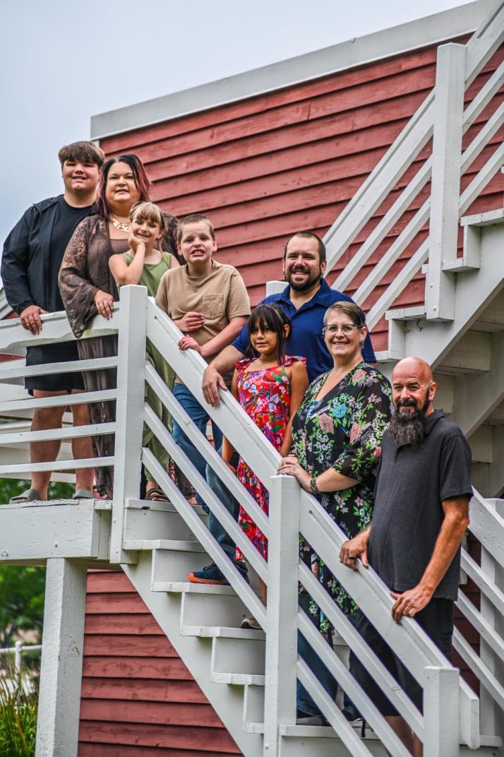 This is a family photo that has 8 people standing on stairs in front of a red building